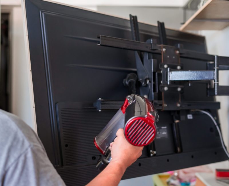 A man vacuum cleaning behind television At Home.