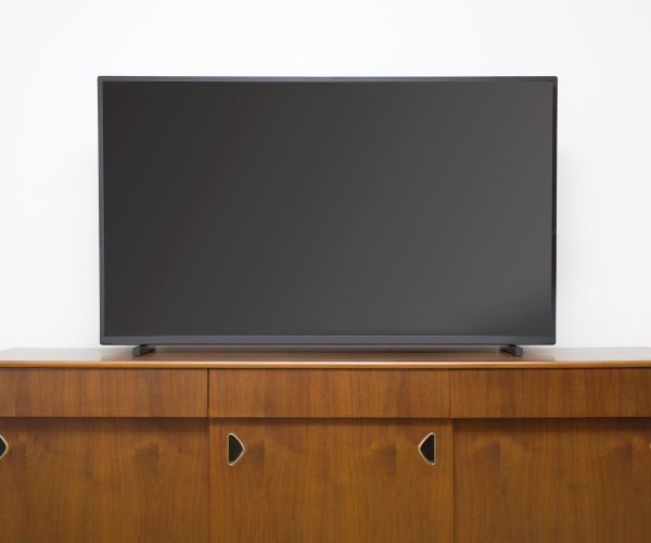Modern TV set with empty blank screen on the wooden cabinet in front of white wall
